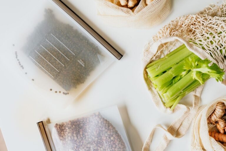 Reusable zip-lock bags filled with lentils and beans laid flat beside celery and ginger