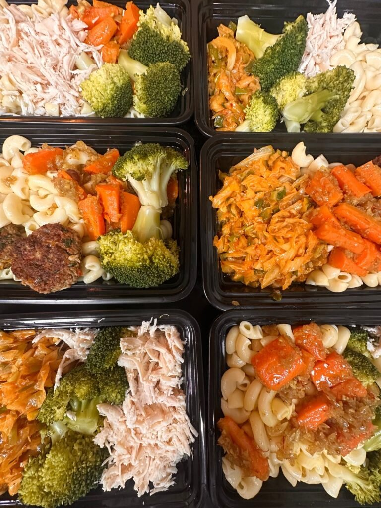 Meal prep trays portioned with shredded chicken, pasta, broccoli, and carrots